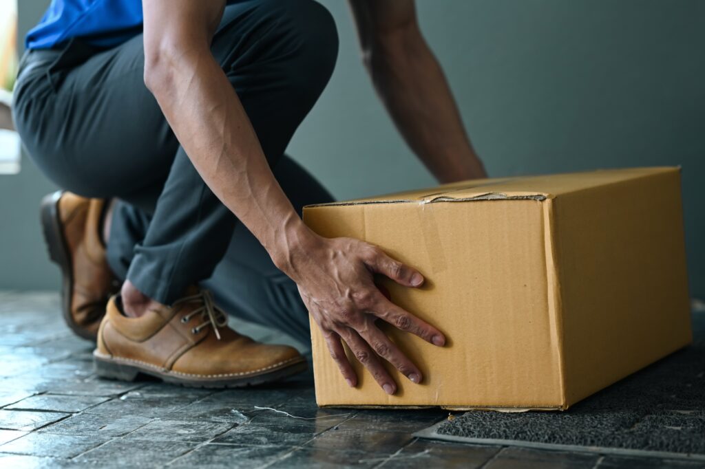Cropped image of male courier putting parcel cardboard box near entrance.