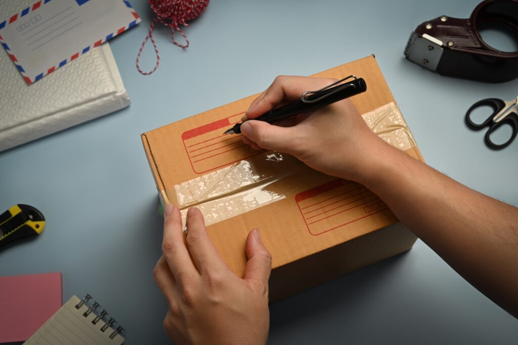 Cropped image of man writing address on carton box.