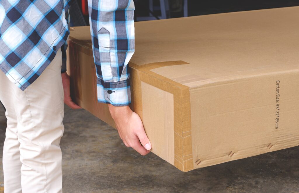 Delivery courier man moving large heavy cardboard box to customer in front of house